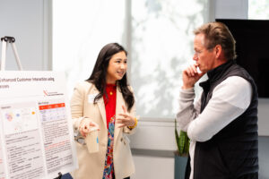 A woman standing beside a research poster and speaking with a man who is listening intently