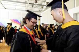 Photo by Ruby Wallau. Graduate Richard Yu laughs with a friend while putting on his academic medal