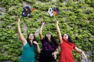 Photo by Ruby Wallau. Three graduates toss their caps