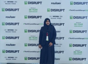 In front of the photo backdrop for TechCrunch Disrupt, Aisha poses for a photo.