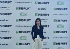 In front of the photo backdrop for TechCrunch Disrupt, Yi poses for a photo.