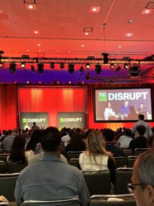 A photo from one of the stages where a panel discussion is happening onstage; the room is lit a dramatic red and the audience is full.