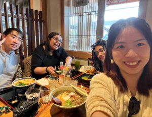 Four people smile around a restaurant table with bowls of ramen