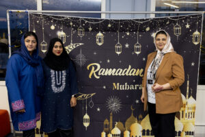 Three women, each dressed nicely for dinner, posing in front of a Ramadan Mubarak photo backdrop