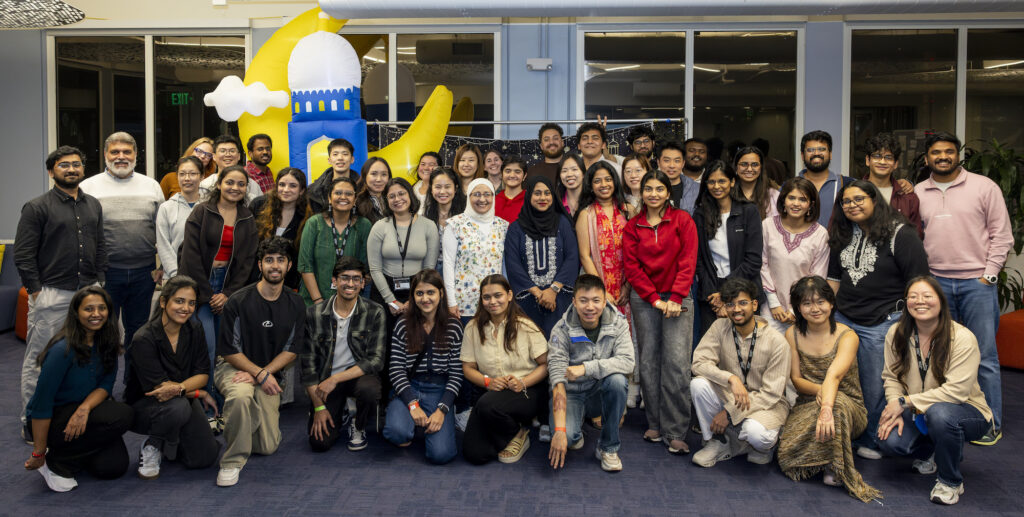 A group photo taken of some of the night's attendees; about 50 people are in the picture arranged in rows with a playful inflated crescent moon backdrop