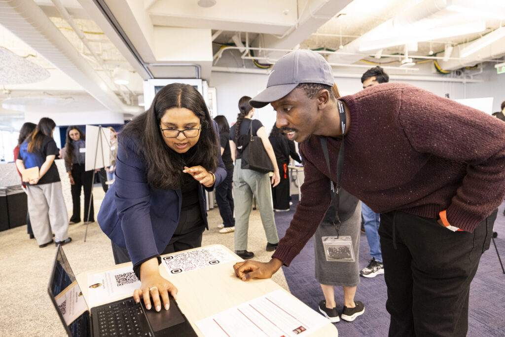 A judge and a student lean in to view a project on a laptop